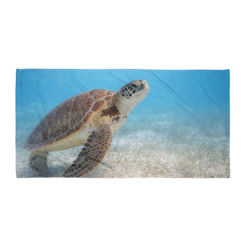 Beach towel displaying a sea turtle swimming through shallow coastal waters.