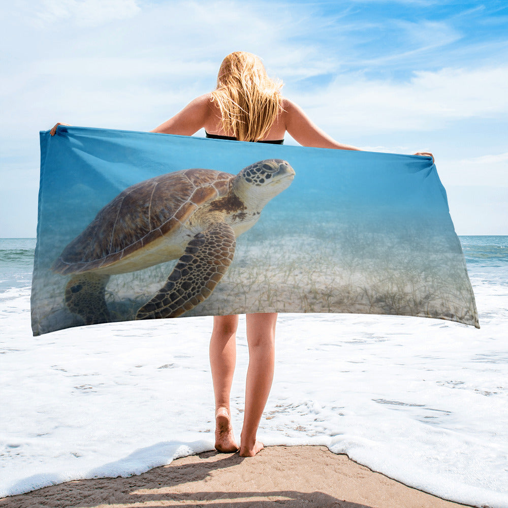 Beach towel displaying a sea turtle swimming through shallow coastal waters.